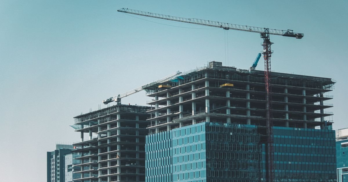 Skyline view of modern skyscrapers under construction with cranes against a clear sky.